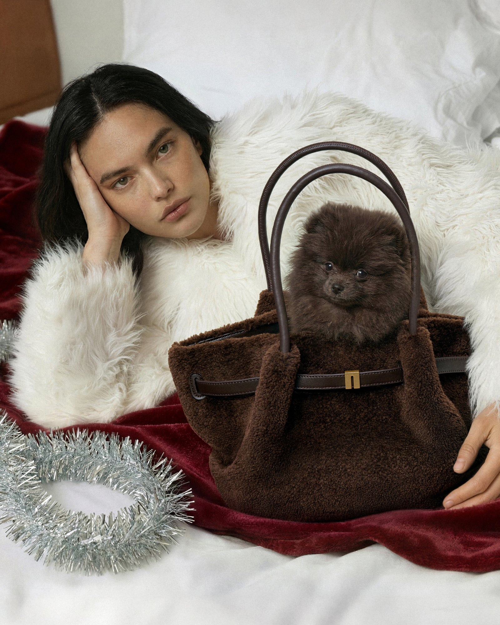 Woman with a fluffy white coat holding a brown handbag with a small dog inside, on a white background.